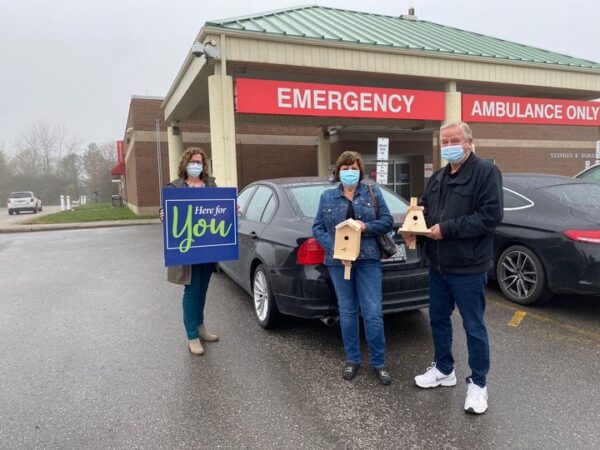 Two individuals holding up birdhouses with Rachel Agnoluzzi who is holding a Here for You campaign poster